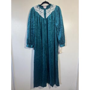 May include: A teal-colored, floor-length robe with long sleeves and a white lace collar. The robe is made of a soft, velvety material and hangs on a black hanger. The collar features a delicate, floral lace design.