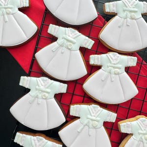 May include: A close-up of nine pink and white decorated sugar cookies shaped like dresses. The cookies are arranged on a black wire rack with a red cloth underneath.