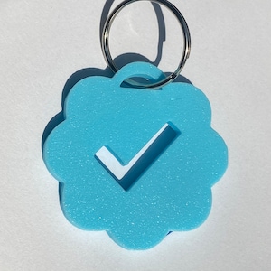 May include: A light blue keychain shaped like a cloud with a white checkmark inside. The keychain has a silver metal ring.