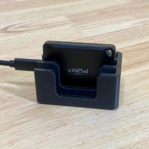 May include: A black external hard drive with a stand and a USB cable. The hard drive has the text "crucial by micron" on it.