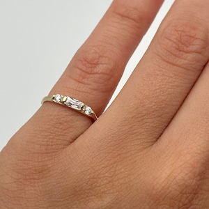 May include: A gold ring with three small diamonds. The ring is on a person's finger.