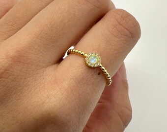 May include: A gold ring featuring a white opal stone set in a halo of smaller clear stones.