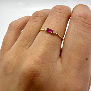 May include: A delicate gold ring with a rectangular ruby gemstone and two smaller round diamonds.