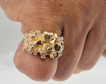 May include: A gold nugget ring with a textured surface. The ring is worn on a person's finger.