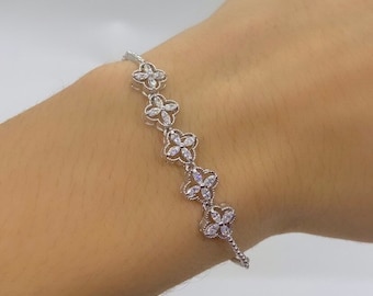 May include: A silver bracelet with a delicate chain and a series of flower-shaped charms set with clear cubic zirconia stones.