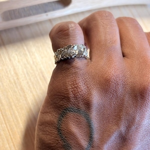 May include: A silver-toned ring with a textured, organic, and irregular surface. The band features a rugged, molten-like appearance with multiple raised, rounded nodes and crevices across its entire circumference, creating a distinct, uneven profile.