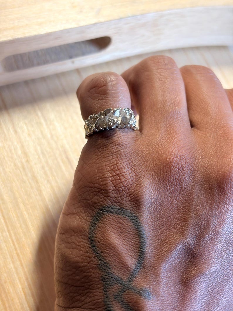 May include: A silver-toned ring with a textured, organic, and irregular surface. The band features a rugged, molten-like appearance with multiple raised, rounded nodes and crevices across its entire circumference, creating a distinct, uneven profile.