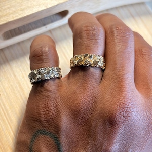May include: Two rings with a textured, nugget-style surface. One ring is silver-toned with a metallic finish, and the other is gold-toned with a metallic finish. Both rings feature an irregular, bumpy design that wraps around the entire band.