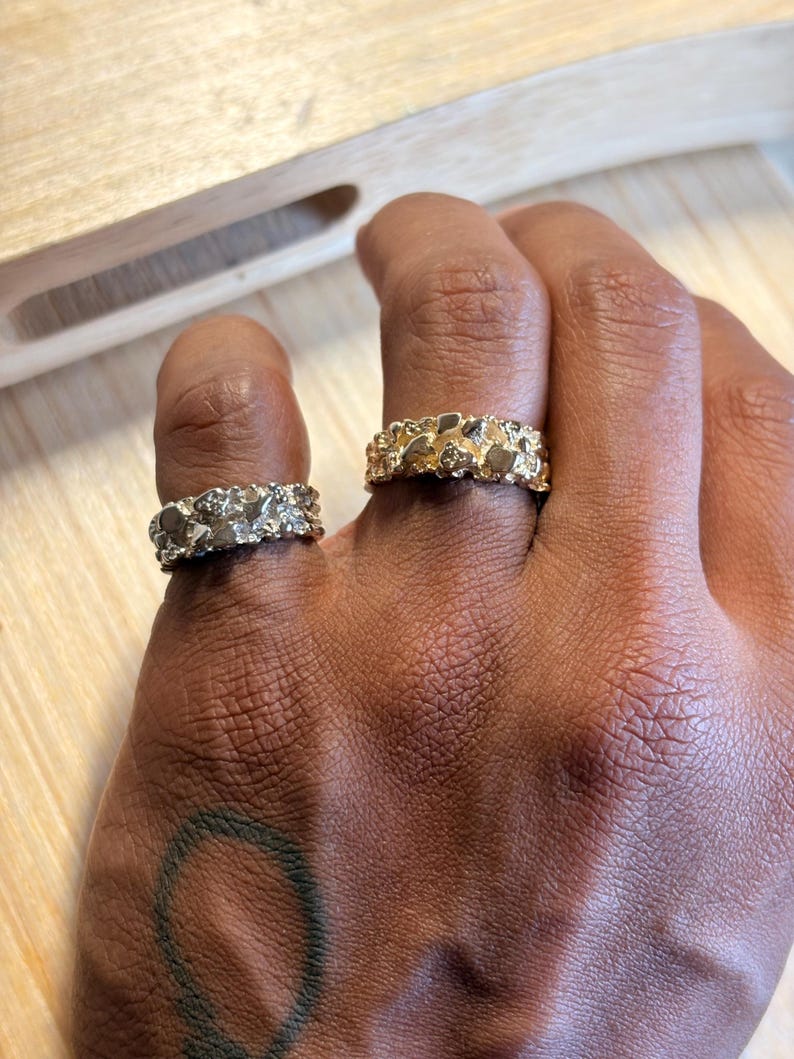 May include: Two rings with a textured, nugget-style surface. One ring is silver-toned with a metallic finish, and the other is gold-toned with a metallic finish. Both rings feature an irregular, bumpy design that wraps around the entire band.