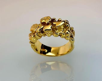 May include: A gold ring featuring a band with a highly textured, irregular surface composed of multiple small, rounded, and raised metallic shapes that create a clustered, organic appearance with a polished, reflective finish throughout.