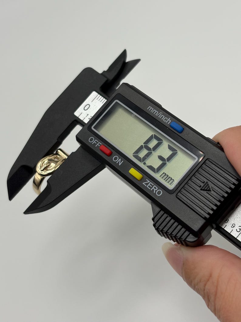 A gold-colored ring is measured with a black digital caliper. The caliper displays a measurement of 8.3 mm.