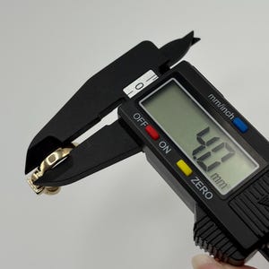 The caliper displays a measurement of 4.7 mm. The ring has a square-shaped stone and a simple band.