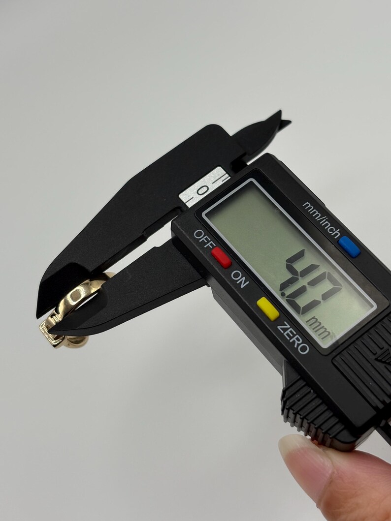 The caliper displays a measurement of 4.7 mm. The ring has a square-shaped stone and a simple band.