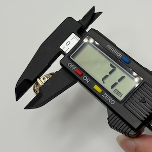 A gold ring is measured with a black digital caliper. The caliper displays a measurement of 7.1 mm.