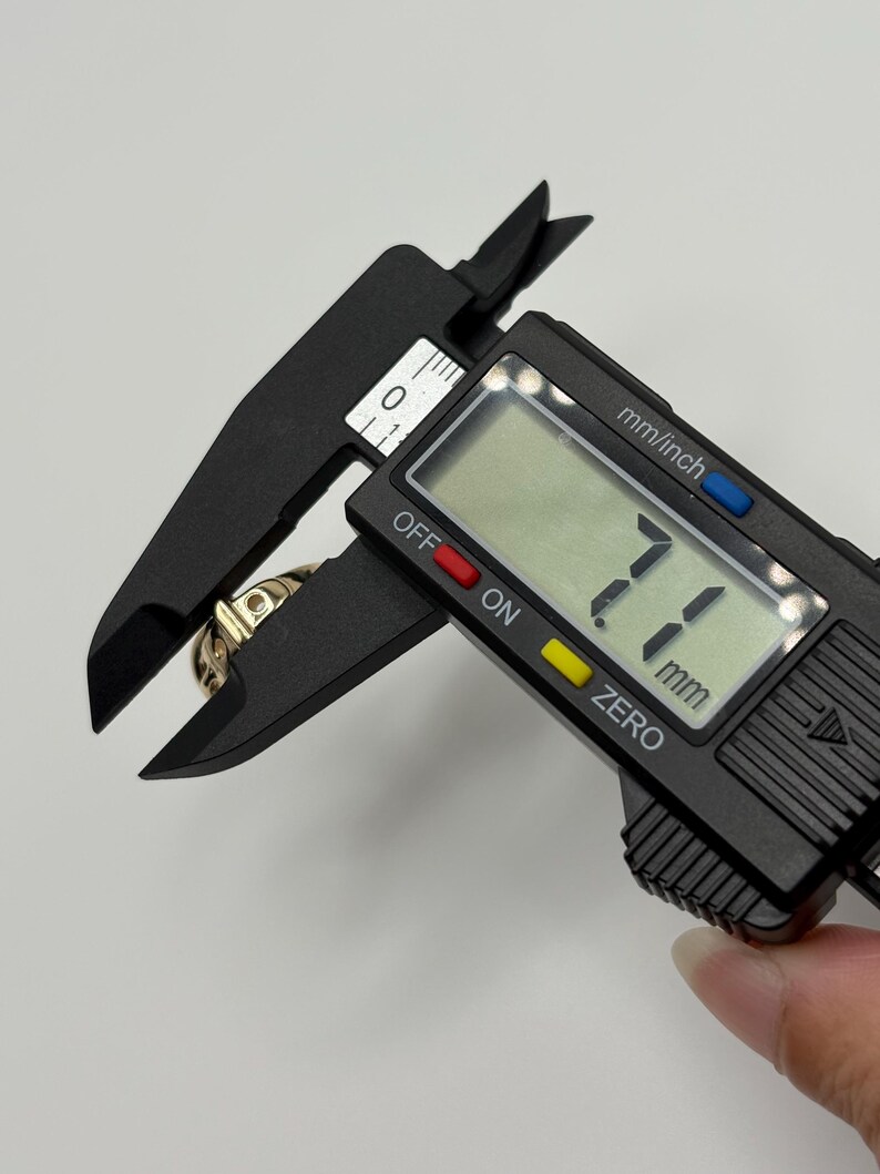 A gold ring is measured with a black digital caliper. The caliper displays a measurement of 7.1 mm.