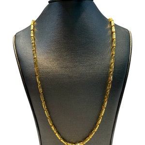 May include: A gold-colored necklace with a rectangular link design is displayed on a black mannequin. The necklace is draped around the mannequin's neck, showcasing its full length and intricate link pattern. The background is plain white.