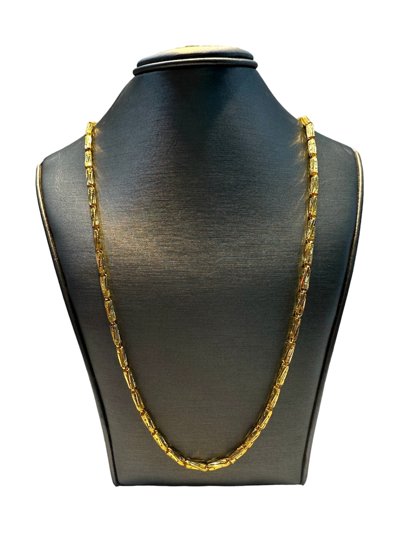 May include: A gold-colored necklace with a rectangular link design is displayed on a black mannequin. The necklace is draped around the mannequin's neck, showcasing its full length and intricate link pattern. The background is plain white.