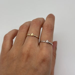 May include: Two simple, delicate Claddagh rings. One ring is gold and the other is silver.