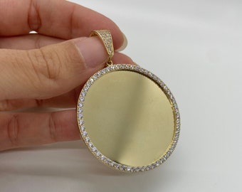May include: A gold round pendant with a smooth, blank surface surrounded by a border of small, clear stones.