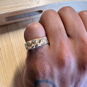 May include: A gold-toned ring featuring a textured, irregular nugget-style surface with a high-shine finish. The band has a wide, chunky profile with raised, organic shapes that create a multi-faceted appearance across the entire outer circumference.