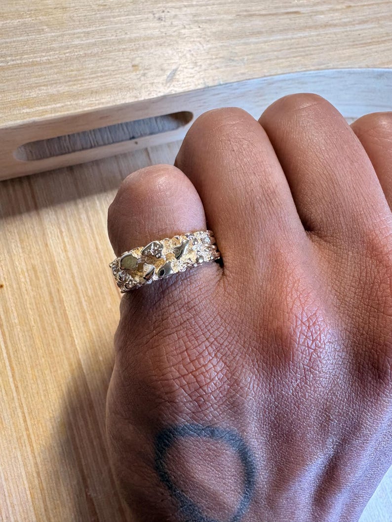 May include: A gold-toned ring featuring a textured, irregular nugget-style surface with a high-shine finish. The band has a wide, chunky profile with raised, organic shapes that create a multi-faceted appearance across the entire outer circumference.