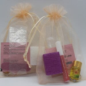 Puede incluir: Dos pequeñas bolsas beige transparentes con cordón llenas de productos para el cuidado de las uñas. Cada bolsa contiene un pequeño frasco de aceite, un tubo de brillo labial, una lima de uñas morada y otros artículos. Las bolsas están sobre un fondo blanco liso.