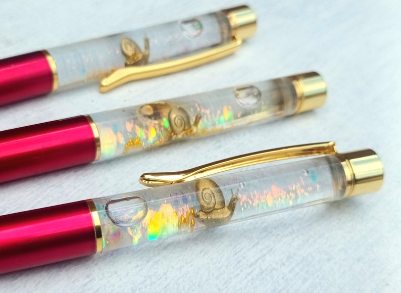 May include: Three red and gold pens with clear barrels filled with iridescent glitter and small snail figurines.