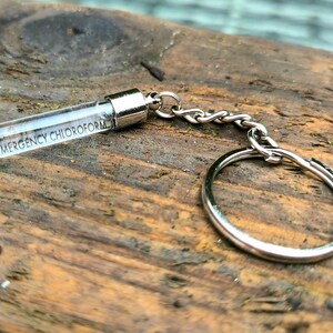 May include: A silver keychain with a clear glass vial that says "EMERGENCY CHLOROFORM" on it.