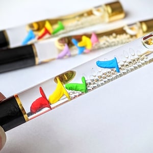 May include: A black and gold pen with a clear barrel filled with colourful floating shapes. The shapes are red, yellow, green, blue, and purple.