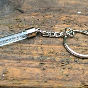 May include: A silver keychain with a clear glass vial that says "EMERGENCY CHLOROFORM" on it.