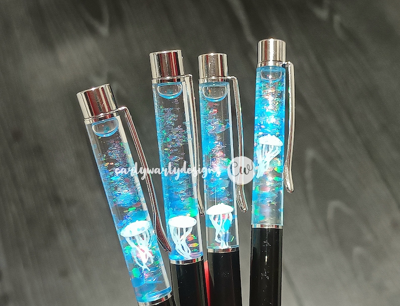 May include: Four clear blue pens with silver caps and black barrels. Each pen contains a white jellyfish and iridescent glitter. The pens are arranged vertically.