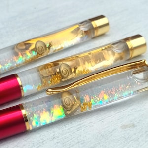 May include: Three red and gold pens with clear barrels filled with iridescent glitter and gold snail charms.