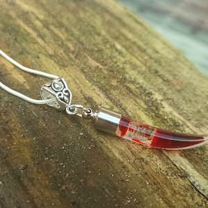 May include: A silver necklace featuring a pendant shaped like a red chili pepper. The pendant is filled with a red liquid and has a silver cap and bail. The chain is a thin, silver snake chain.