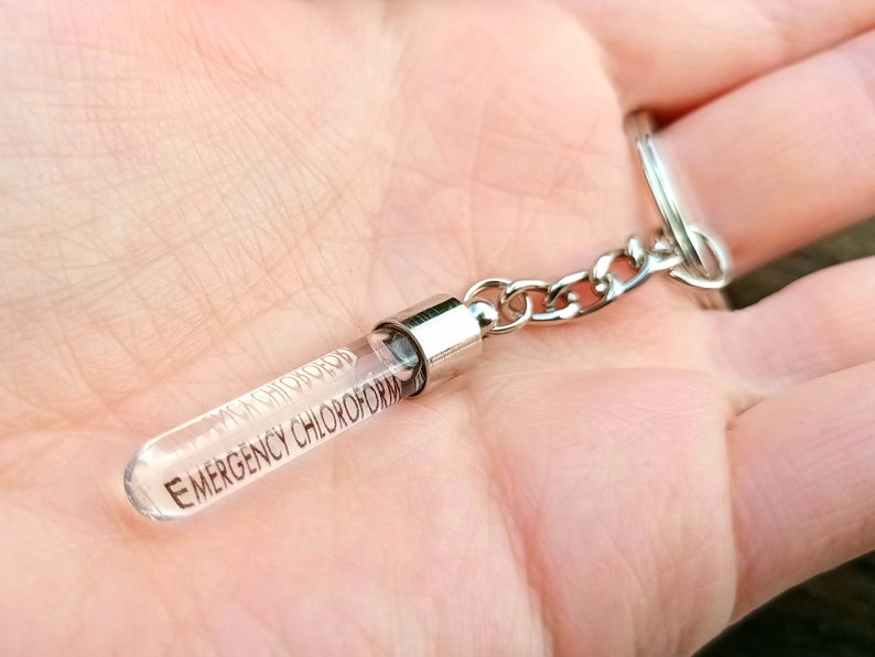 May include: A silver keychain with a clear glass vial attached. The vial has the text "EMERGENCY CHLOROFORM" printed on it.