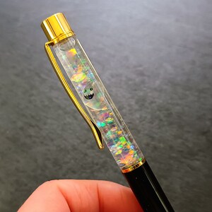 May include: A gold and black pen with a clear barrel filled with iridescent glitter and a small ghost graphic.
