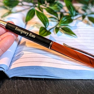 May include: A black and orange pen with a silver tip and a gold inscription that reads "Emergency Rum".
