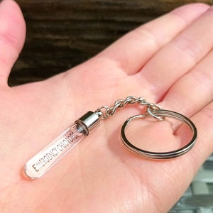May include: A silver keychain with a clear glass tube that says "Emergency Contact" on it.