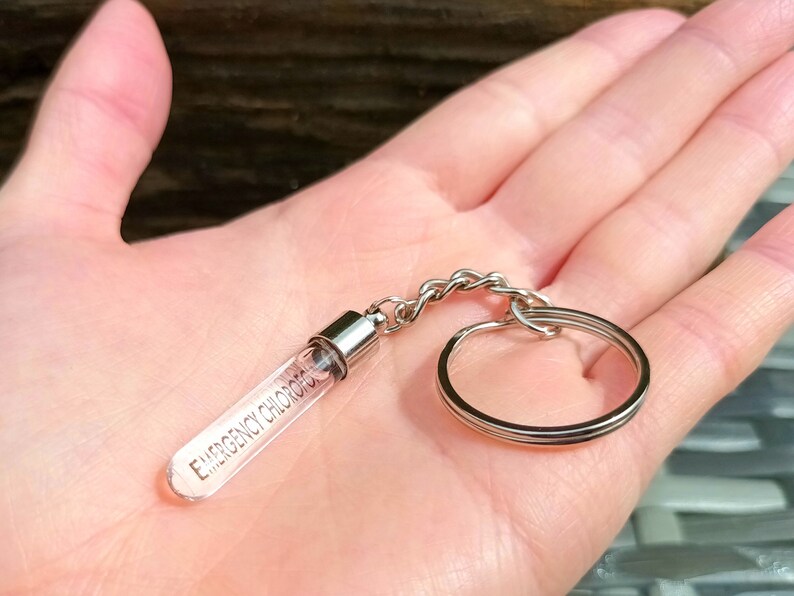 May include: A silver keychain with a clear glass tube that says "Emergency Contact" on it.