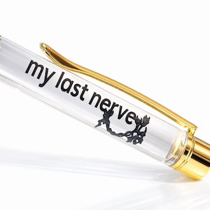 May include: A black and gold pen with the text "my last nerve" printed on the clear barrel. The pen has a gold clip and accents, and a black top.
