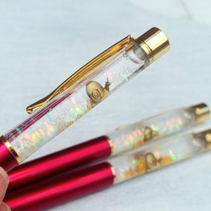 May include: Three red and gold pens with clear barrels filled with iridescent glitter and a gold snail charm.