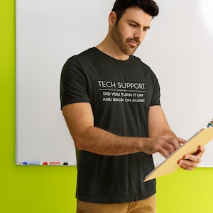 May include: A man wearing a black t-shirt with the text "Tech Support Did you turn it off and back on again?" printed in white. He is holding a clipboard and looking down at it.