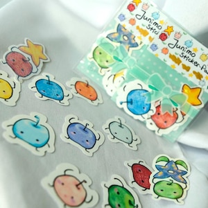 May include: A collection of colorful Junimo stickers, featuring various fruit-like characters with smiling faces. Some stickers are loose, while others are packaged in a clear plastic sleeve with the text "Junimo Sticker-Pack".