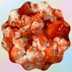 May include: Close-up of gourmet popcorn with a vibrant orange and white coating. The popcorn kernels are clustered together, showcasing the texture and color contrast. The image is set against a soft, pastel-colored background.