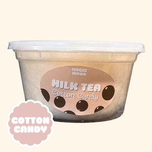 May include: A clear plastic container filled with light brown cotton candy. The container has a label that says "MAGIC WAND MILK TEA Cotton Candy".
