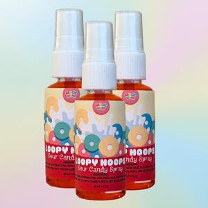 May include: Three bottles of Loopy Hoops Sour Candy Spray with white spray nozzles. The labels feature colorful cartoon designs of cereal hoops and the text "Loopy Hoops Sour Candy Spray". The liquid inside is a vibrant orange.