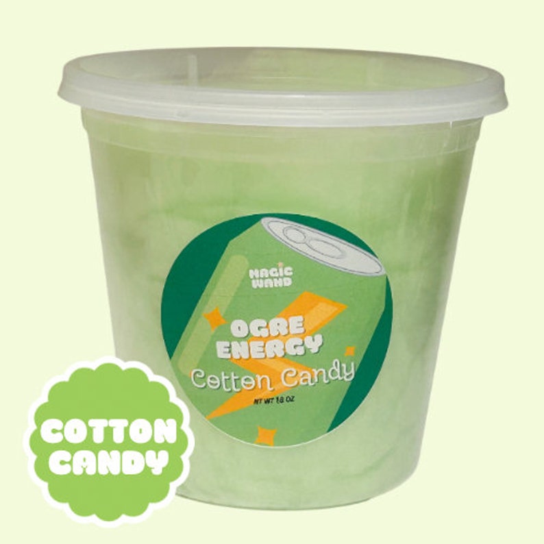 May include: A large plastic container filled with green candy floss. The container has a clear lid and a round sticker with the words "Ogre Energy Cotton Candy" and a graphic of a soda can. A green scalloped sticker reads "Cotton Candy".