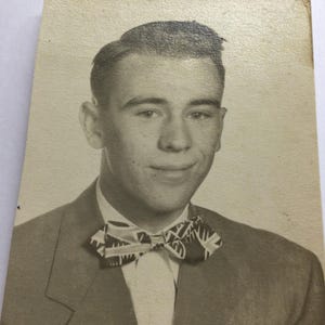 May include: Black and white portrait of a young person wearing a suit jacket, white shirt, and patterned bow tie. The photograph is a vintage image, with a slightly aged appearance.
