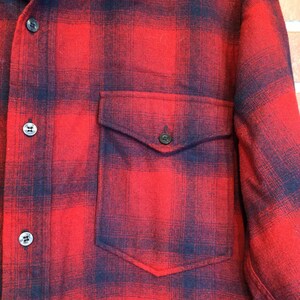 May include: Red and black plaid flannel shirt with a button-down front and a single chest pocket. The shirt has black buttons and a classic lumberjack style.