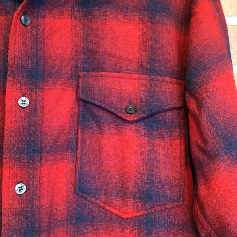 May include: Red and black plaid flannel shirt with a button-down front and a single chest pocket. The shirt has black buttons and a classic lumberjack style.