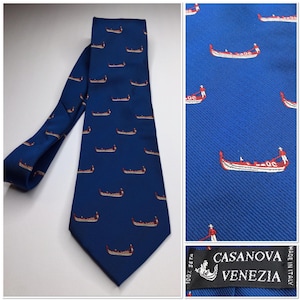 May include: A navy blue silk tie featuring a repeating pattern of gondolas in red and white. The tie is labeled "CASANOVA VENEZIA" and is made of 100% seta. The tie is a classic accessory for formal or business attire.